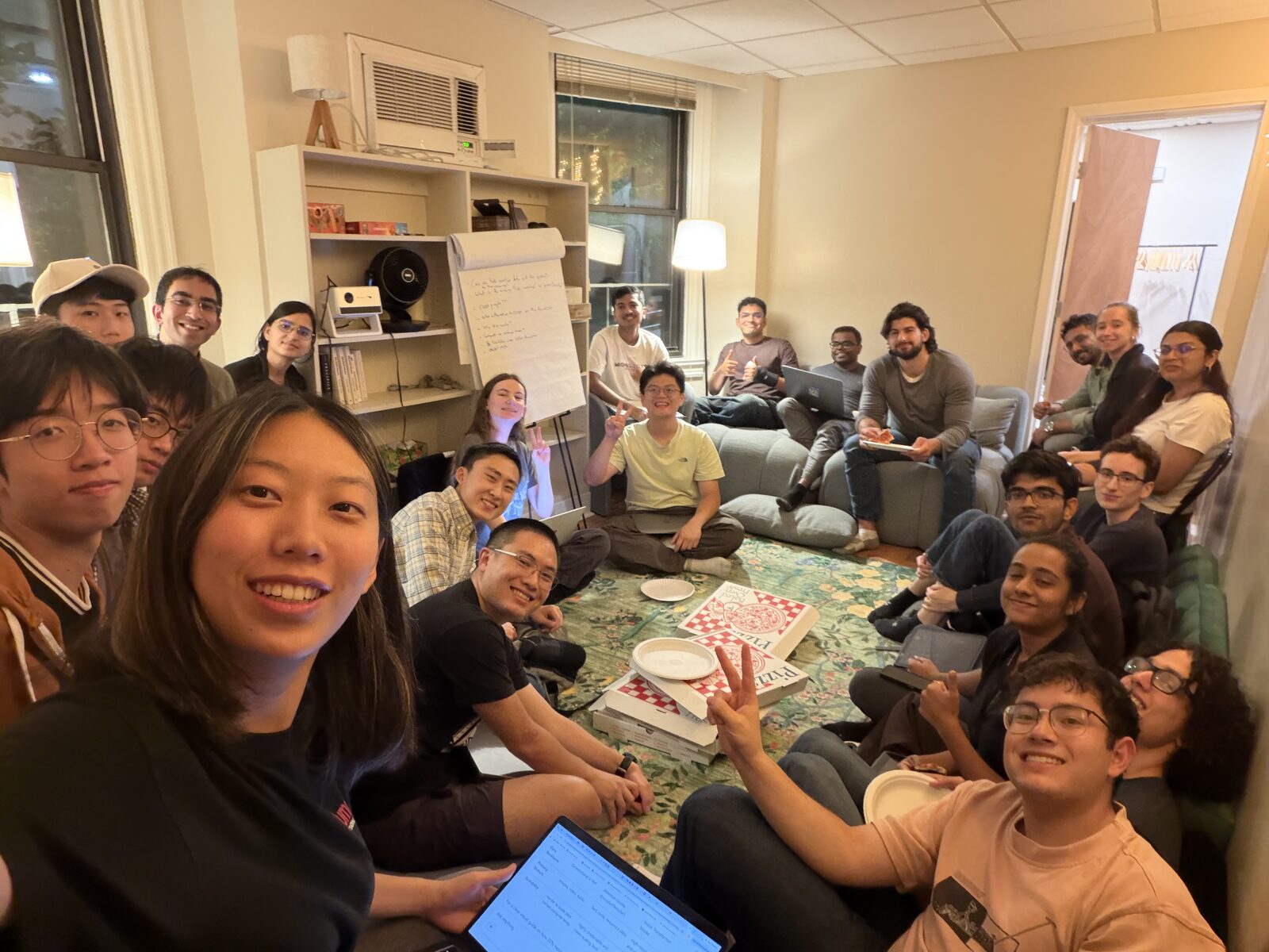 MLn Reading Club, Week 14 — the group ringed around the rug at CASI, pizza boxes in the middle, with the evening's questions on the flip chart behind them